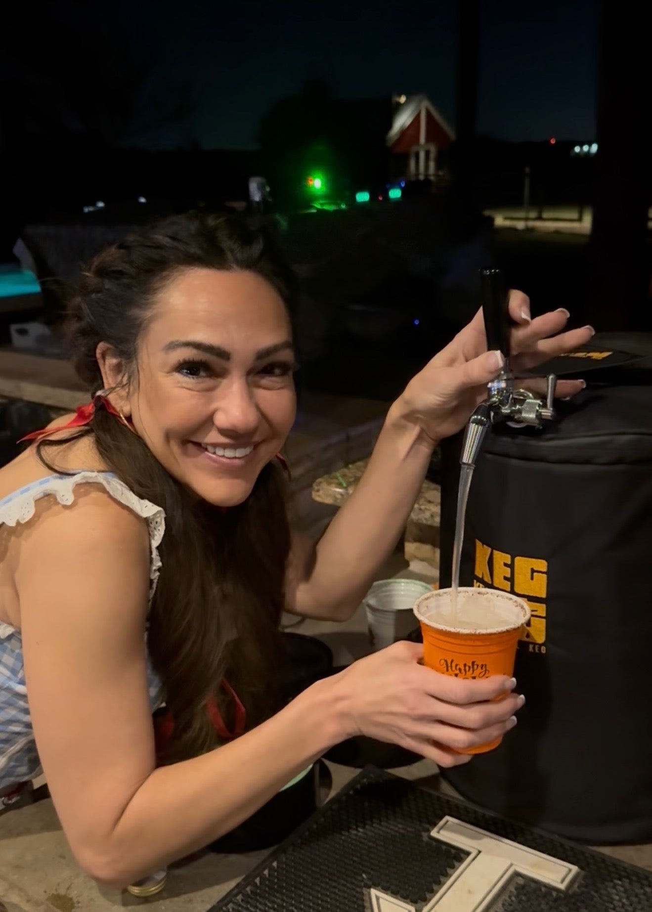 Woman holding a cup pouring a drink from a Keg It Keg Kit outdoors at a party at night